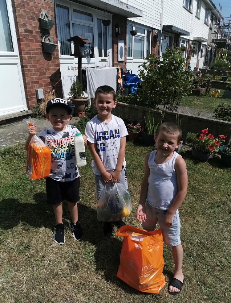 smiling children hold bags of food in their front garden